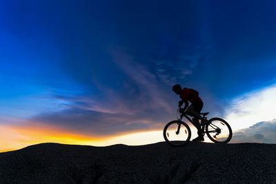 Silhouette man riding bicycle against sky during sunset