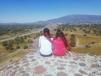 Rear view of women sitting on mountain against sky