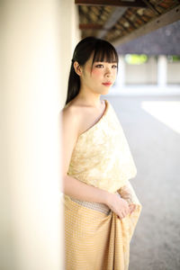 Woman looking away while standing against wall