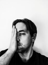 Portrait of man covering face with hand against white background