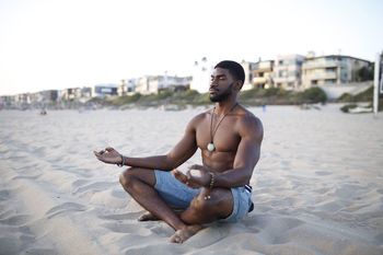 Shirtless muscular man meditating at beach against clear sky