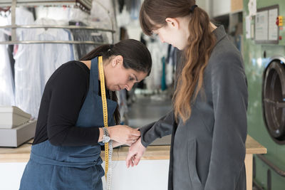 Side view of mature female tailor adjusting overcoat sleeve for young customer