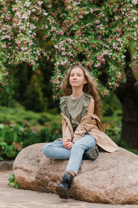 Beautiful teen girl with long blonde hair sits on a rock in the park person