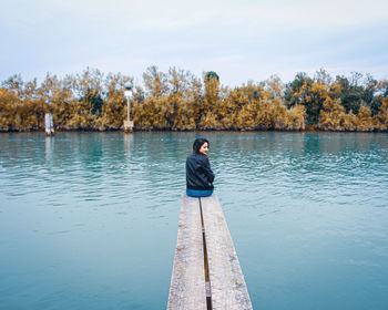 Young woman sitting amidst lake on jetty during autumn