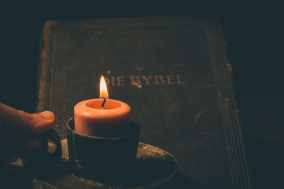 Cropped hand of person holding lit candlestick by bible darkroom