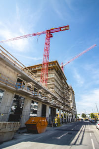 Low angle view of crane by building against sky