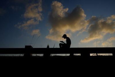 Silhouette man standing on bridge against sky during sunset