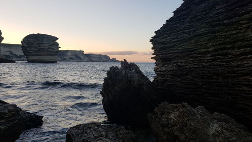 Rock formations on beach against sky during sunset