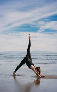 Full length of young woman jumping on sea against sky