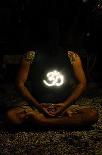 Midsection of man sitting in illuminated park at night