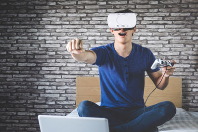 Young man looking through virtual reality simulator while sitting on bed at home