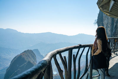 Rear view of woman standing on railing against mountain