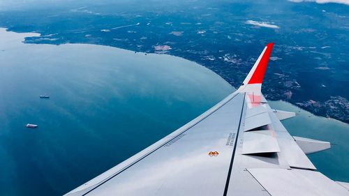 Close-up of aircraft wing flying over sea against blue sky