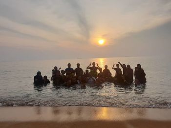 People enjoying in sea against sky during sunset