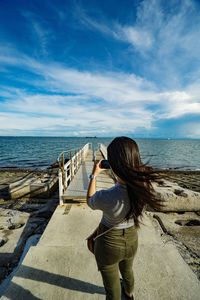 Rear view of woman standing at beach against sky