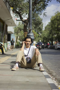 Portrait of young man sitting on street in city