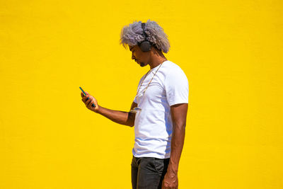 Man holding umbrella while standing against yellow wall