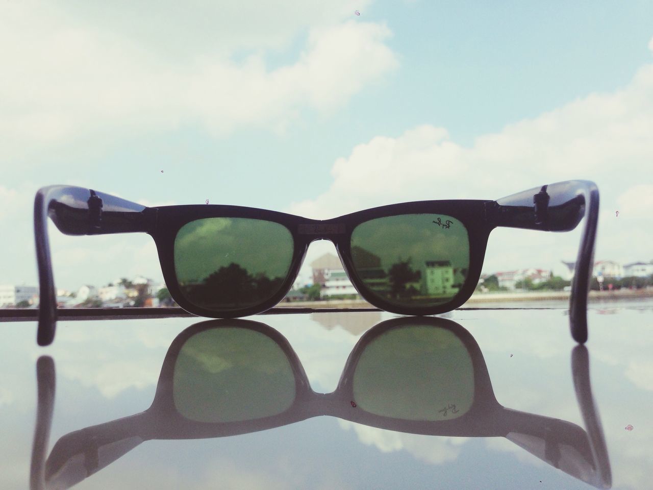 CLOSE-UP OF SUNGLASSES AGAINST CLOUDS