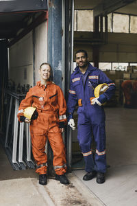 Smiling male and female coworkers in protective workwear at factory warehouse