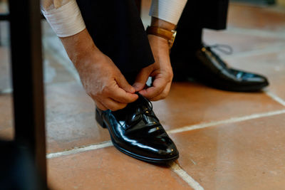 Low section of man tying shoelace on tiled floor