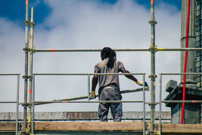 Rear view of man working on railing against sky