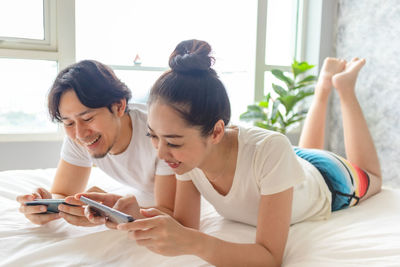 Young woman using smart phone on bed at home