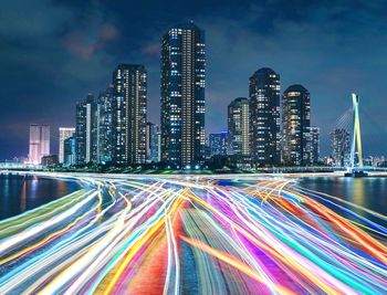 Light trails on city buildings against sky at night