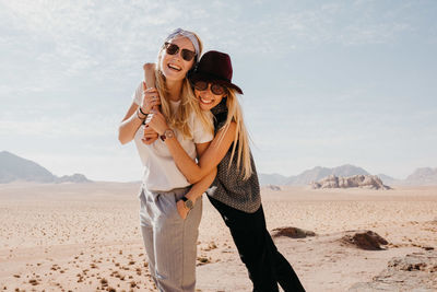 Happy friends wearing sunglasses standing on desert against sky