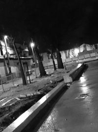 Empty road by illuminated buildings in city at night