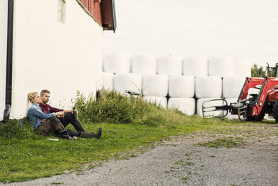 Couple relaxing on grassy field by road against hay bales