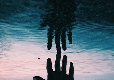 Cropped hand touching water in lake during sunset
