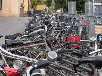 Many old bicycles padlocked to the rack near train station.