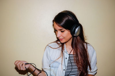 Young woman listening to music against wall