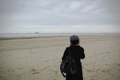 Rear view of man standing at beach against sky