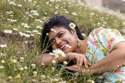 A cheerful smiling indian girl lying on field full of calendula flowers looks away