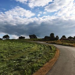 Empty road by grassy field against cloudy sky