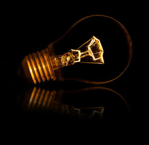 Close-up of illuminated light bulb against black background