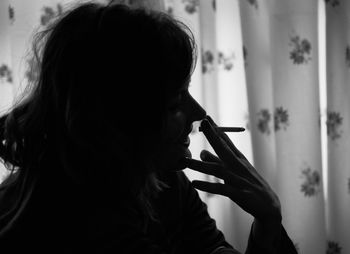 Close-up of silhouette woman smoking cigarette at home
