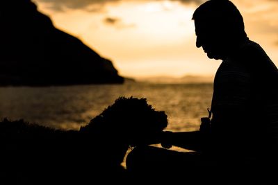 Silhouette of man with dog by sea against sky during sunset
