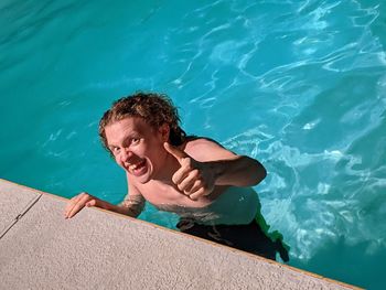 High angle view of teenage boy swimming in pool making a funny face and thumb up sign