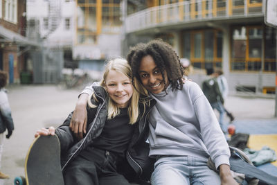 Smiling girls sitting together with arm around in school campus