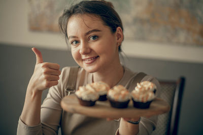 Young woman shows cool with cupcakes in  hand. cream decoration. bakery chef bakes cakes in kitchen