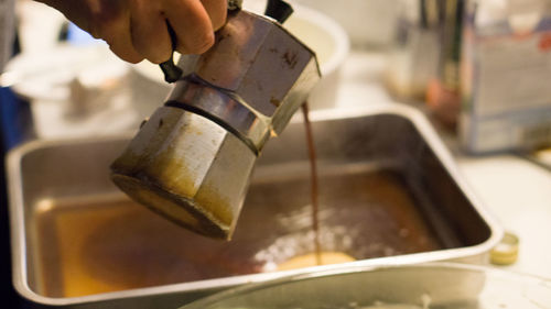 Close-up of hand pouring coffee in container from espresso maker