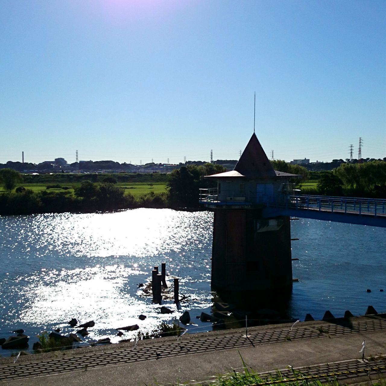 clear sky, water, copy space, blue, built structure, architecture, building exterior, lake, river, reflection, tranquility, transportation, sunlight, outdoors, tranquil scene, nature, day, nautical vessel, pier, scenics