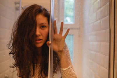 Portrait of woman by through wet glass window