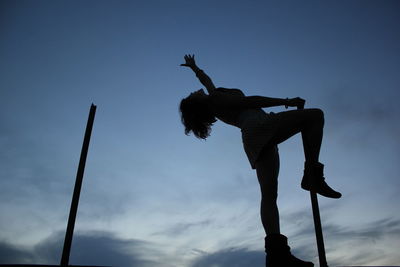 Low angle view of silhouette man jumping on pole against sky