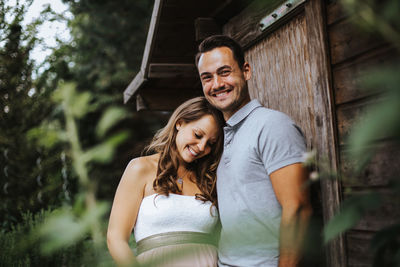 Low angle portrait of romantic couple standing against trees at park