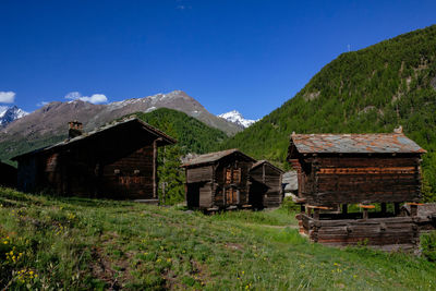 Houses on field by mountain against blue sky