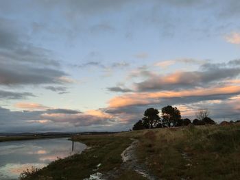 Scenic view of lake against cloudy sky during sunset