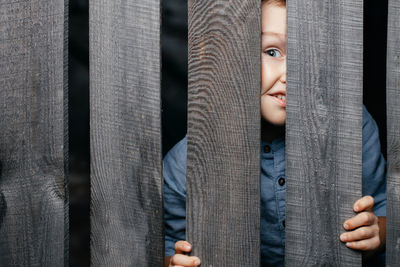 Happy smiling white boy looks out of the crack of a wooden fence. childish curiosity. espionage